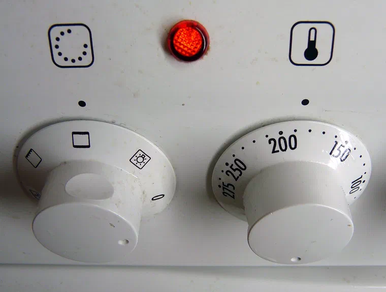 Les boutons d'un four électrique blanc, celui de droite gradué en degrés Celsius de 50 à 250, voyant de chauffe allumé